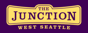 A yellow sign with the words "The Junction" and "West Seattle" in bold purple letters on a purple background.