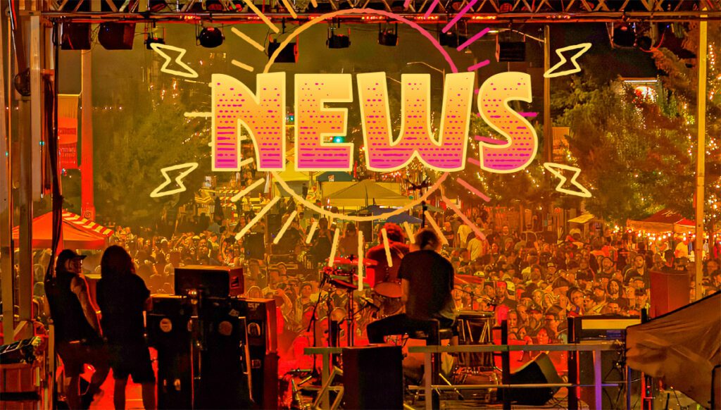 A band performs on an outdoor stage at night before a large crowd, with "NEWS" brightly lit in large letters above the stage.