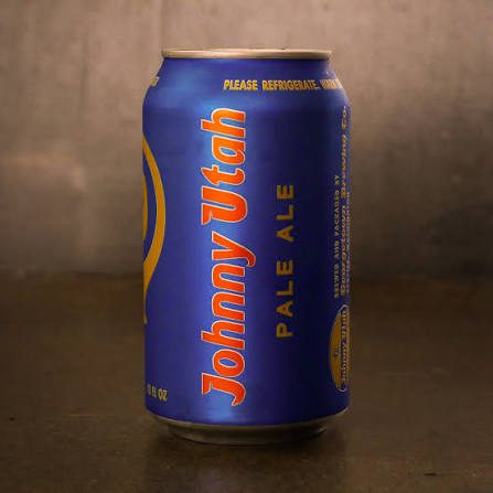 A blue can of Johnny Utah Pale Ale is placed on a dark surface with text and branding visible on the label.